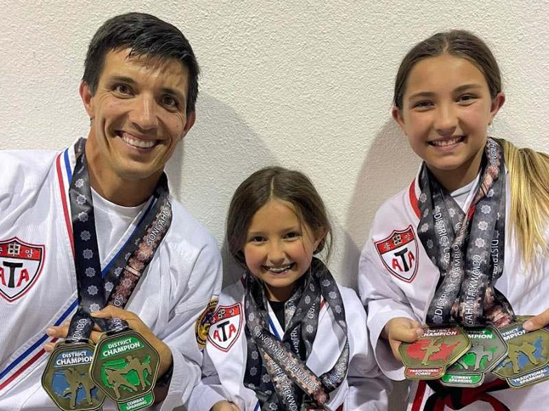 An instructor and two students in ATA uniforms hold district champion medals.